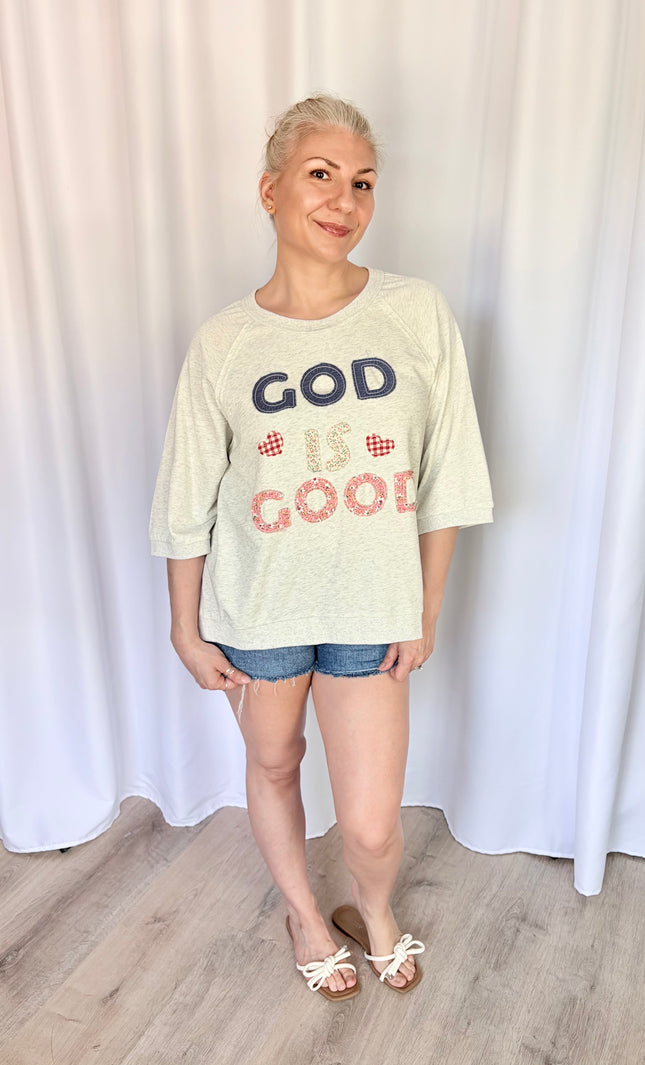 Front view of a model wearing a loose, casual French terry top featuring a vintage-inspired "God is Good" patchwork design across the chest and comfortable 3/4 length raglan sleeves.