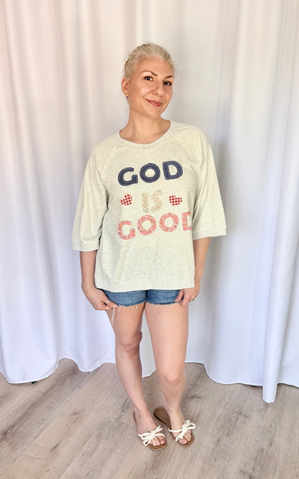 Front view of a model wearing a loose, casual French terry top featuring a vintage-inspired "God is Good" patchwork design across the chest and comfortable 3/4 length raglan sleeves.