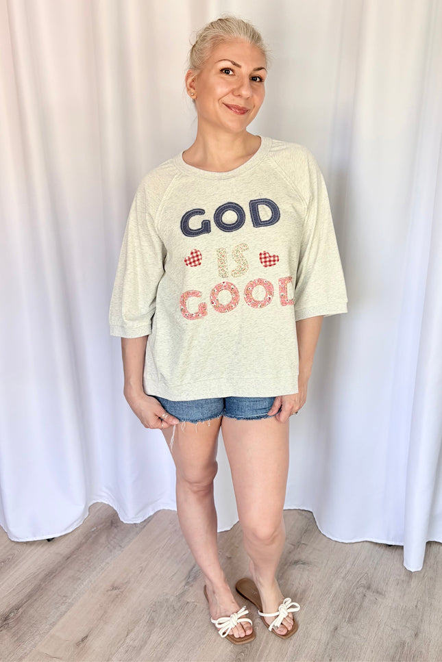 Front view of a model wearing a loose, casual French terry top featuring a vintage-inspired "God is Good" patchwork design across the chest and comfortable 3/4 length raglan sleeves.