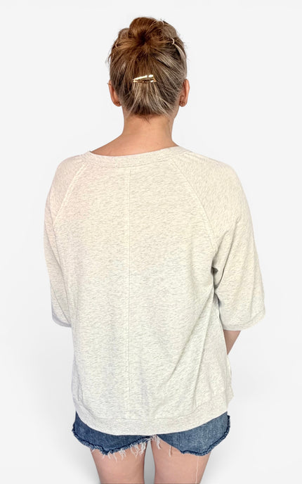 A woman viewed from behind wearing a cream-colored, relaxed-fit crewneck sweatshirt and denim shorts against a plain white 