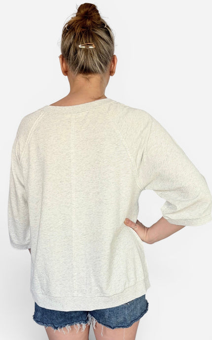 A woman viewed from behind wearing a cream-colored, relaxed-fit crewneck sweatshirt and denim shorts against a plain white background.