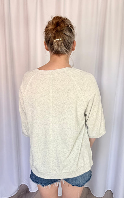 A close-up back view from the waist up, focusing on the clean finish of the round crew neckline and the diagonal raglan sleeve seams extending from the collar to the underarms.