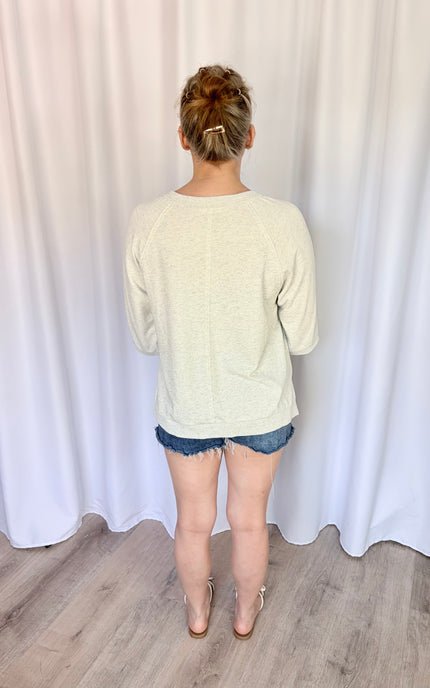 Full-length back view of a model wearing the relaxed-fit French terry top paired with casual bottoms, highlighting how the flat-knit banded hem rests loosely below the waist for an effortless look.