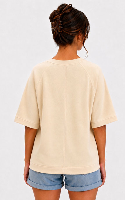 A woman viewed from the back wearing a cream-colored short-sleeve crewneck t-shirt and denim shorts against a plain white background.