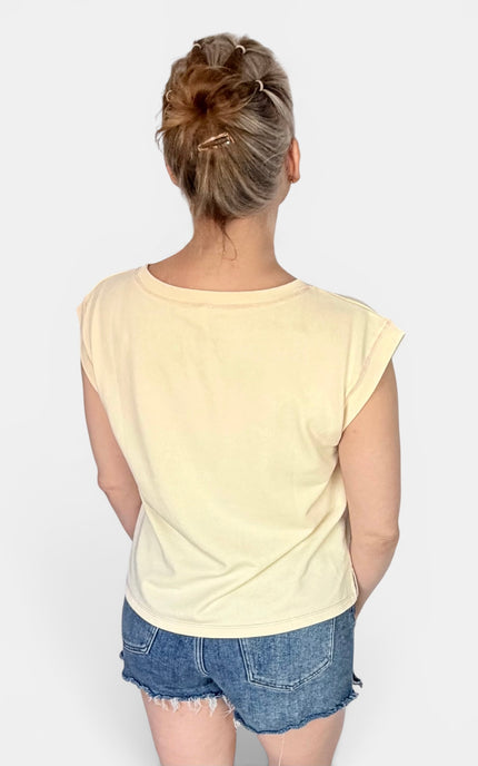 A woman viewed from behind wearing a pale yellow short-sleeve crop top and blue denim shorts against a light gray studio background.