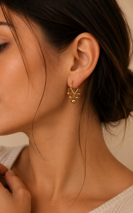 Woman wearing open V-shaped 18k gold hoop earrings with polished dangling ball beads for a modern, elegant look.