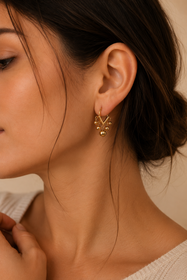 Woman wearing open V-shaped 18k gold hoop earrings with polished dangling ball beads for a modern, elegant look.