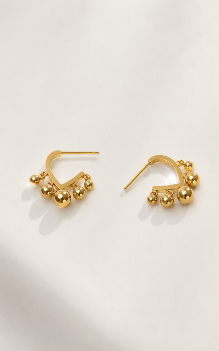 Open V-shaped gold hoop earrings with dangling ball beads styled for an elegant everyday look.