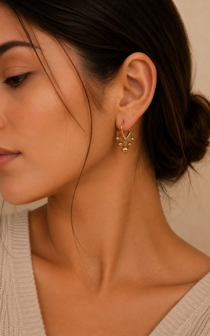 Woman wearing open V-shaped 18k gold hoop earrings with polished dangling gold ball beads for a timeless everyday look.