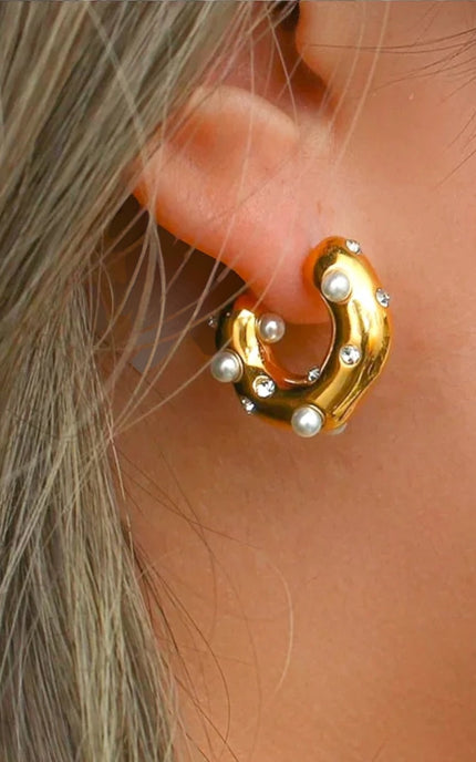 Gold hoop earring with pearl-like stones worn by a person.