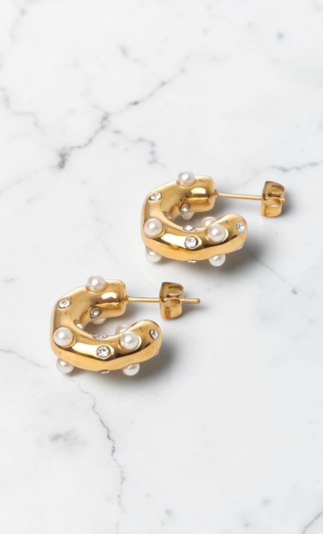 Gold hoop earrings with pearl-like beads on a marble surface