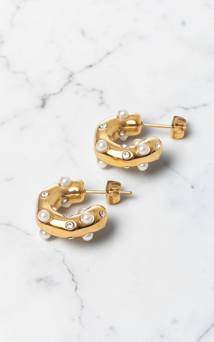 Gold hoop earrings with pearl-like beads on a marble surface