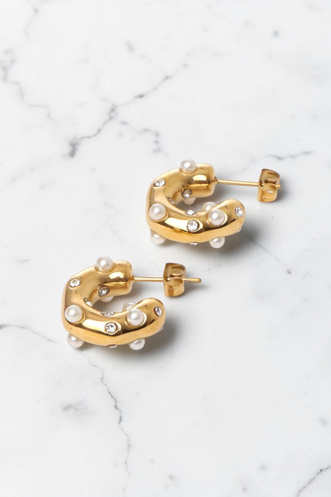 Gold hoop earrings with pearl-like beads on a marble surface