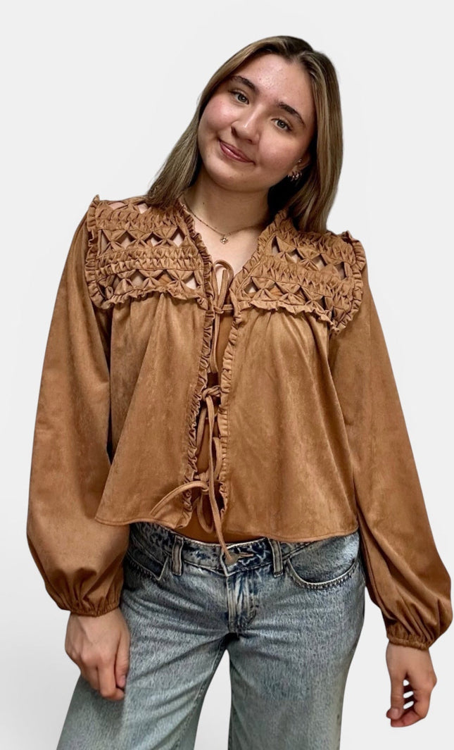Cropped tan suede-like blouse with a large crocheted lace yoke and tie-front detailing, paired with light-wash blue jeans, against a plain light gray studio background.