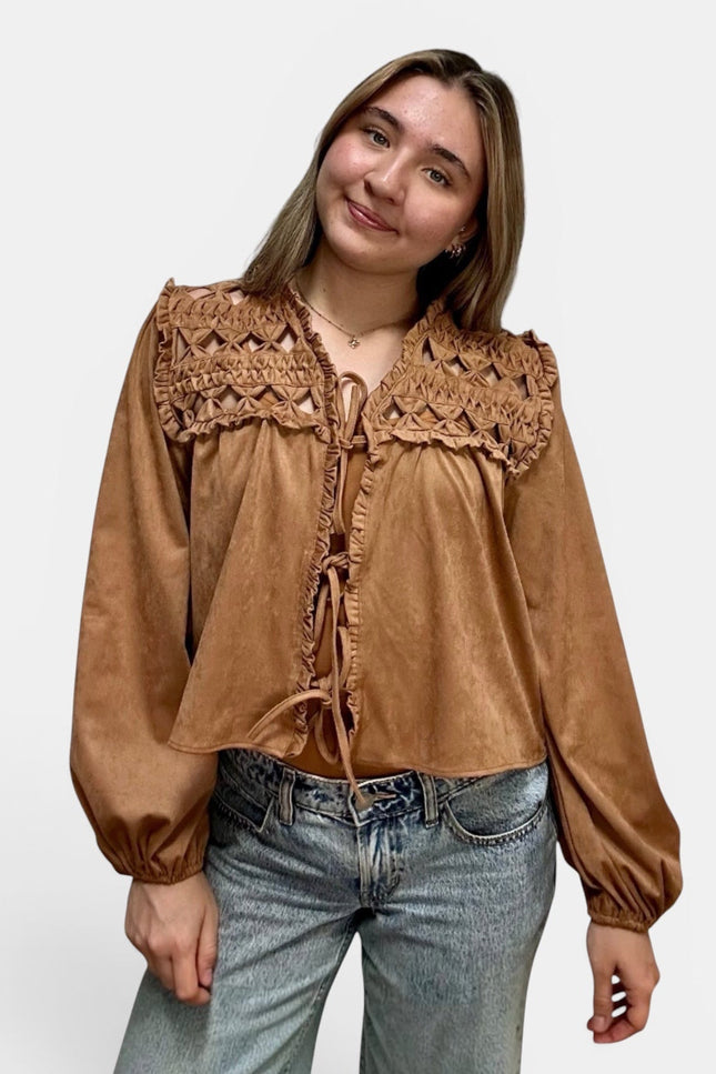 Cropped tan suede-like blouse with a large crocheted lace yoke and tie-front detailing, paired with light-wash blue jeans, against a plain light gray studio background.