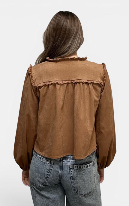 A woman viewed from the back wearing a brown long-sleeve blouse with ruffled trim and light-wash blue jeans against a plain light gray background.