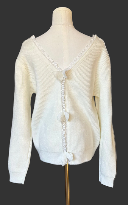 Off-white ribbed sweater with lace-trim V-neckline and oversized bow detail draping down the back, photographed on a Soft Linen background for Justyna Grace Boutique.