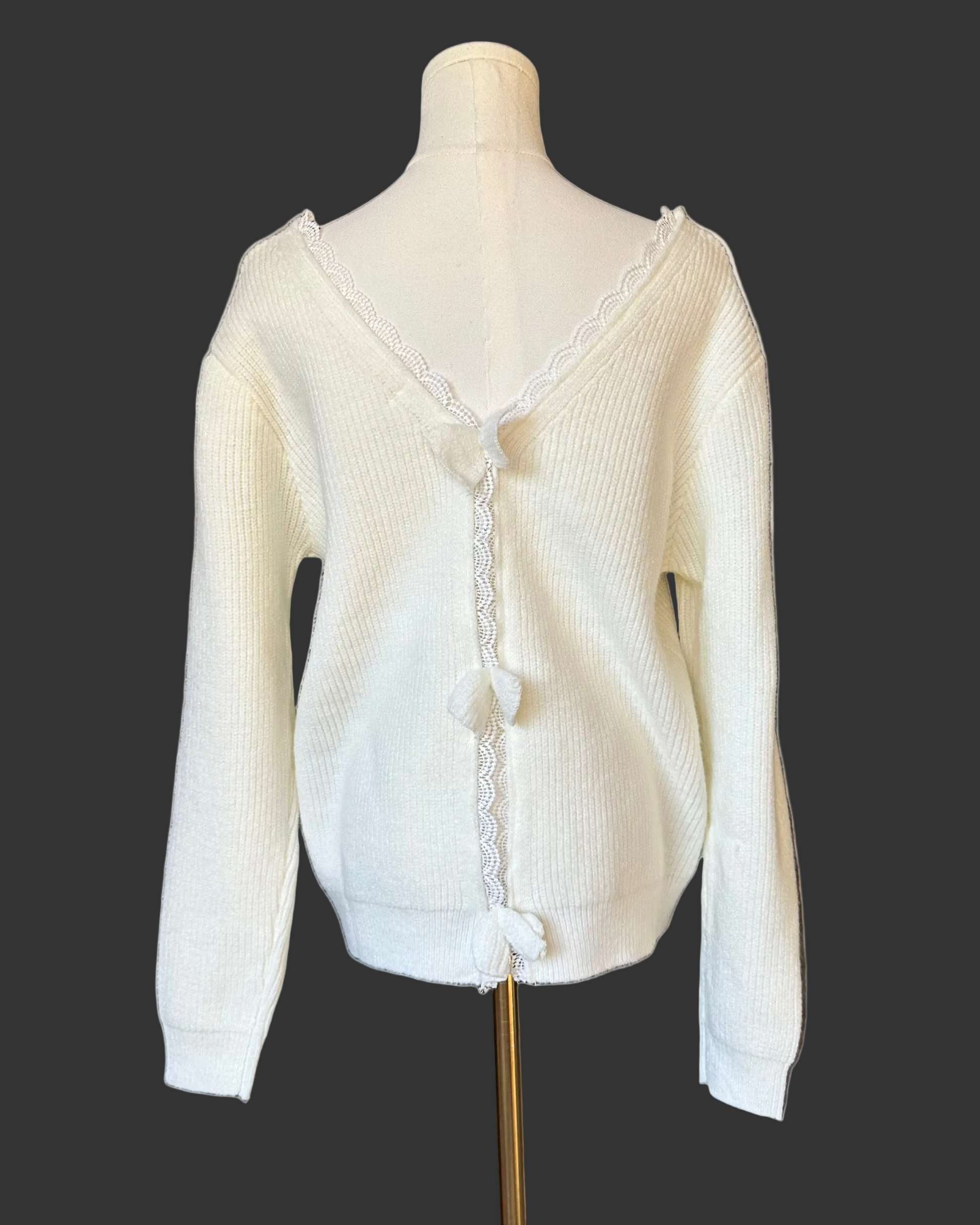 Off-white ribbed sweater with lace-trim V-neckline and oversized bow detail draping down the back, photographed on a Soft Linen background for Justyna Grace Boutique.