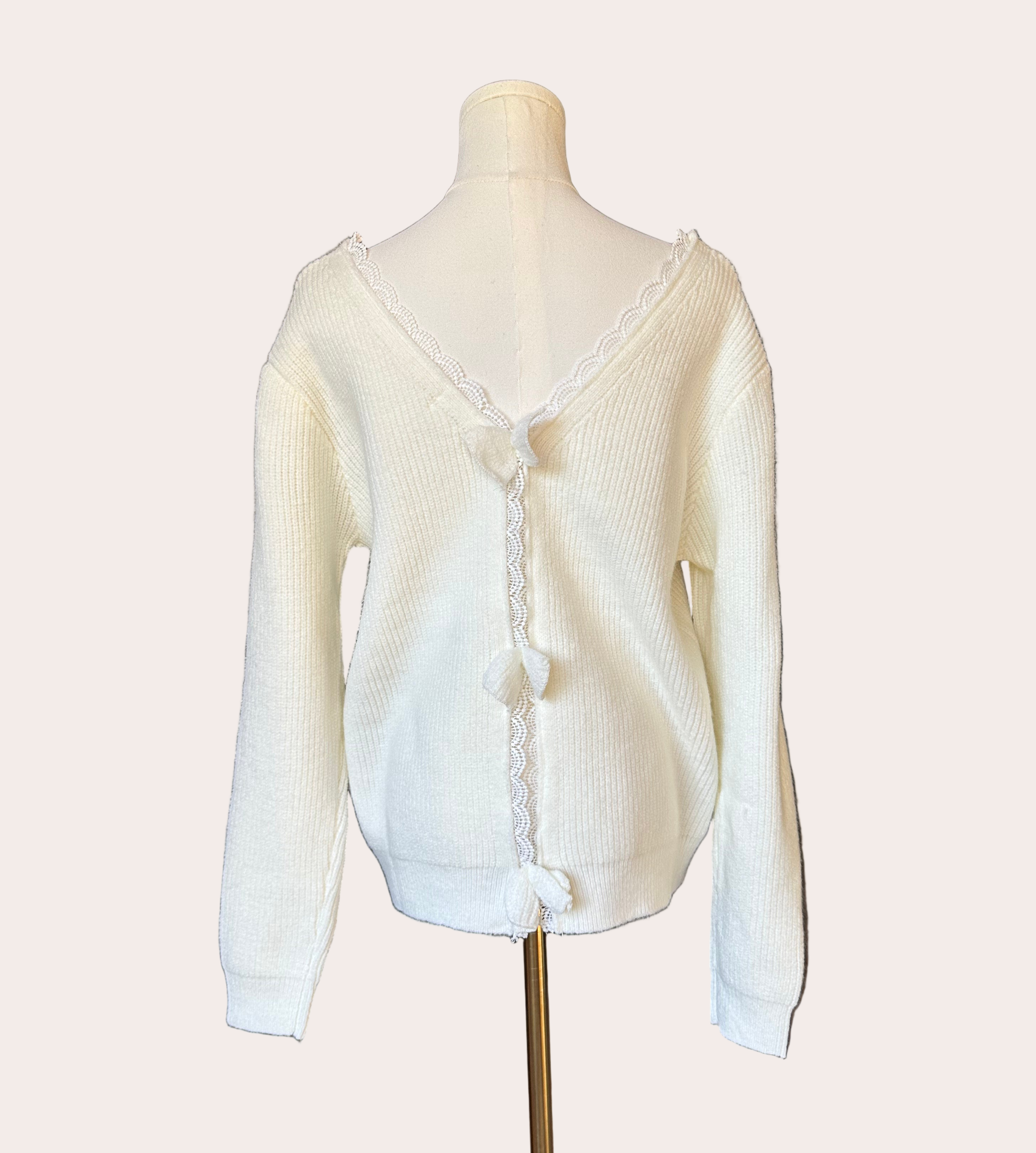 Off-white ribbed sweater with lace-trim V-neckline and oversized bow detail draping down the back, photographed on a Soft Linen background for Justyna Grace Boutique.