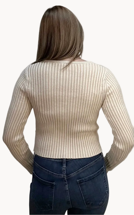 Woman wearing a beige ribbed sweater and blue jeans on a plain background