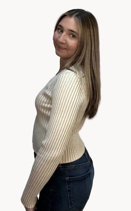 Woman wearing a beige ribbed sweater and dark jeans on a light pink background