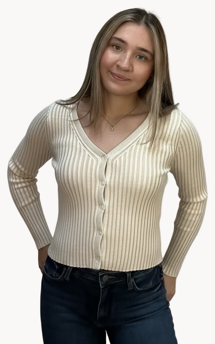 Woman wearing a beige ribbed cardigan over a white shirt with dark jeans on a light pink background