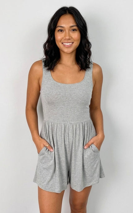 A woman modeling a light gray heather sleeveless romper with a scoop neckline and side pockets, standing against a light gray studio background.