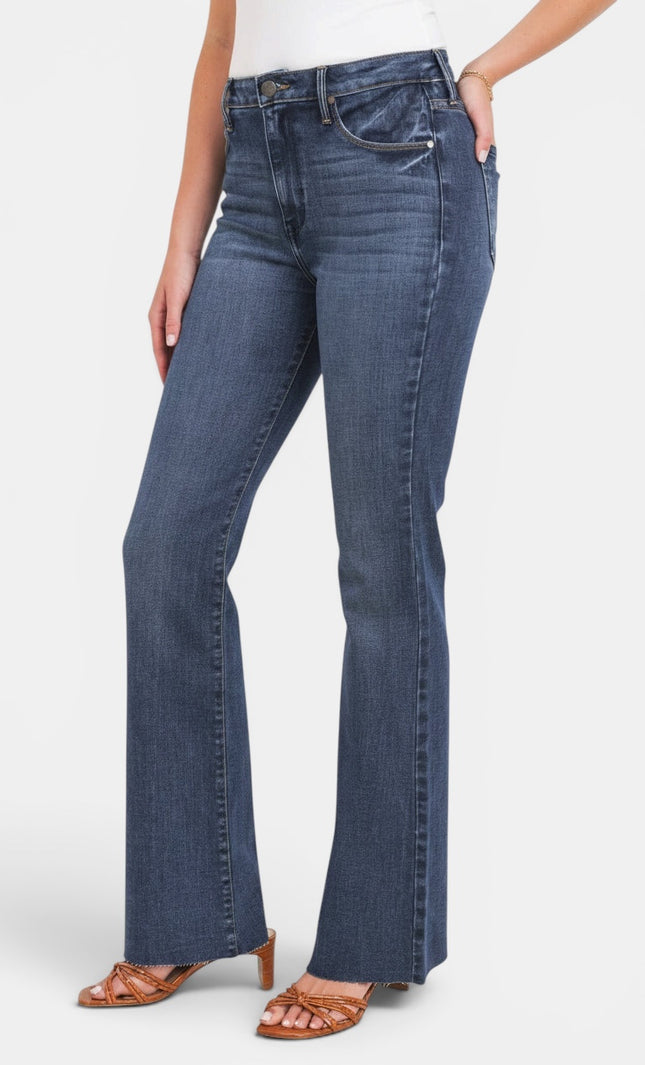 A model wearing a pair of medium-wash blue flare jeans with a white top and brown heeled sandals, shown from the waist down against a light gray studio background.