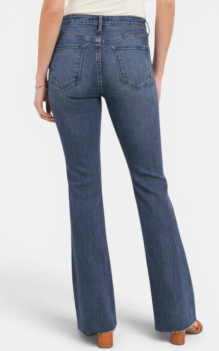 Rear view of a person wearing blue denim flare jeans with a cream top and brown heeled sandals against a light gray studio background.