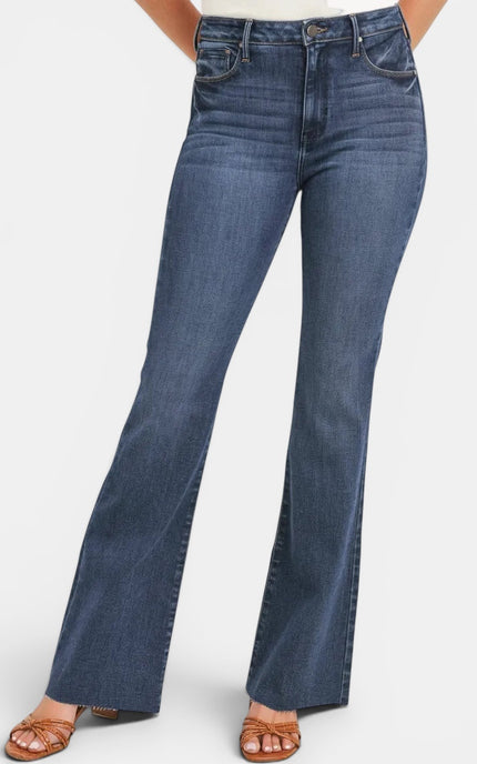 A person wearing medium-wash blue flare jeans with a straight-to-wide leg silhouette, paired with brown strappy sandals against a plain light gray studio background.