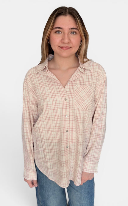 A woman modeling a long-sleeve button-up shirt with a beige and pink plaid pattern, paired with blue jeans, against a plain white background.