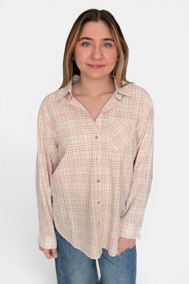 A woman modeling a long-sleeve button-up shirt with a beige and pink plaid pattern, paired with blue jeans, against a plain white background.