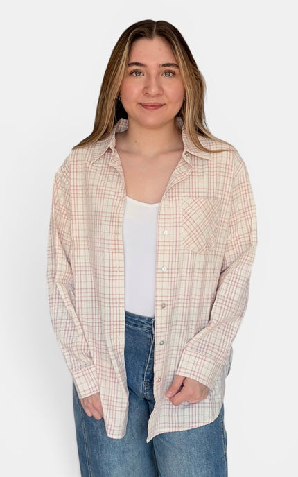 A woman modeling a long-sleeve button-up plaid shirt in beige and white, worn open over a white tank top and blue jeans, against a plain white background.
