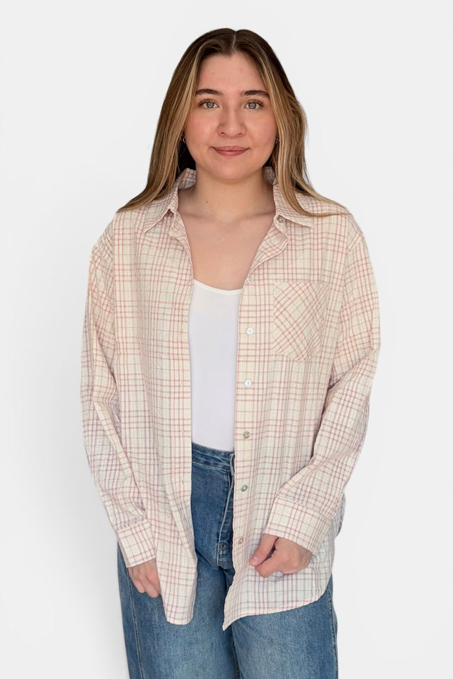 A woman modeling a long-sleeve button-up plaid shirt in beige and white, worn open over a white tank top and blue jeans, against a plain white background.