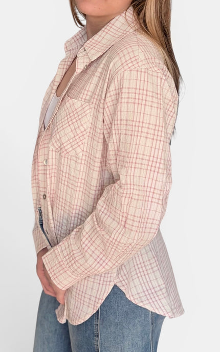 A woman wearing a light beige plaid button-up shirt with a subtle pink and white grid pattern, paired with blue jeans, shown from a side profile view against a plain white background.
