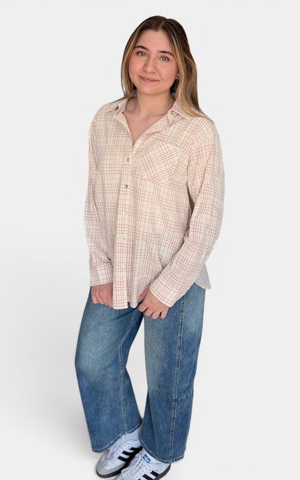 A woman modeling a beige and white plaid button-down shirt with blue jeans and white sneakers, standing against a plain white studio background.