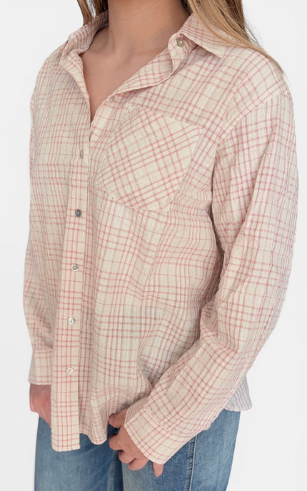 A woman wearing a long-sleeve button-up shirt with a red and beige plaid pattern, paired with blue jeans, shown from the neck down against a plain white background.