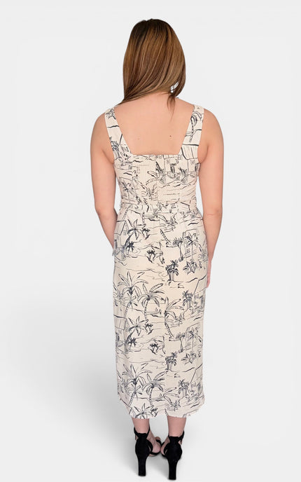 A woman viewed from the back wearing a sleeveless midi dress with a beige base and black botanical line print, paired with black high heels, against a light gray studio background.