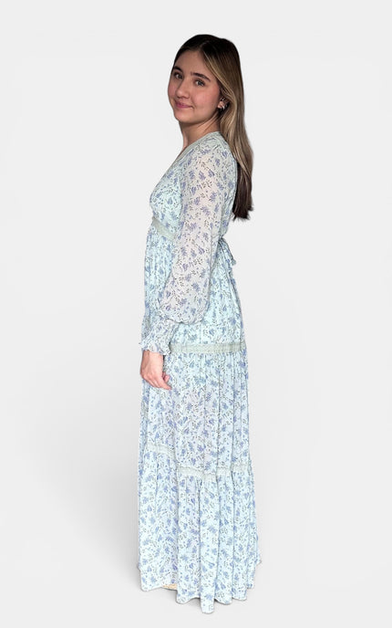 Side view of long-sleeved maxi dress with a light blue and white floral pattern, shown from a side-back angle against a plain light gray studio background.