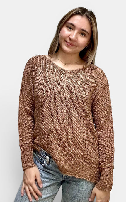 A woman wearing a brown textured knit sweater and blue jeans, standing against a plain light gray background.