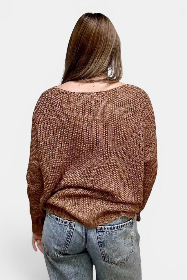 A woman viewed from the back wearing a brown textured knit sweater and light blue jeans against a plain light gray background.