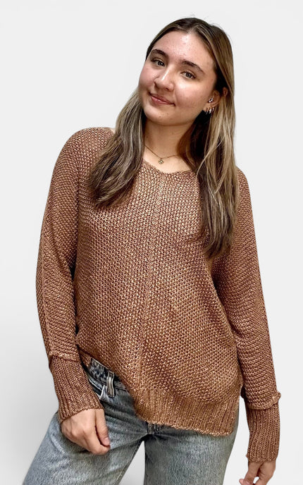 A woman wearing a brown textured knit sweater and light wash jeans, standing against a plain light gray background.