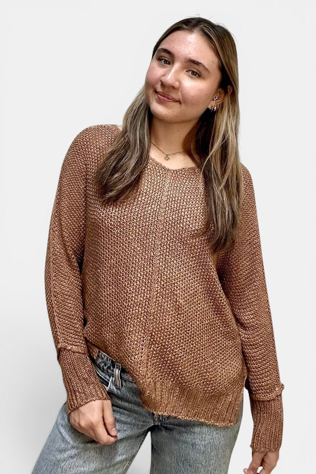 A woman wearing a brown textured knit sweater and light wash jeans, standing against a plain light gray background.