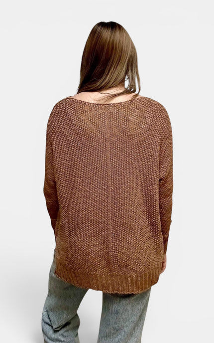 A woman viewed from behind wearing a brown textured knit sweater and light blue jeans against a plain light gray background.