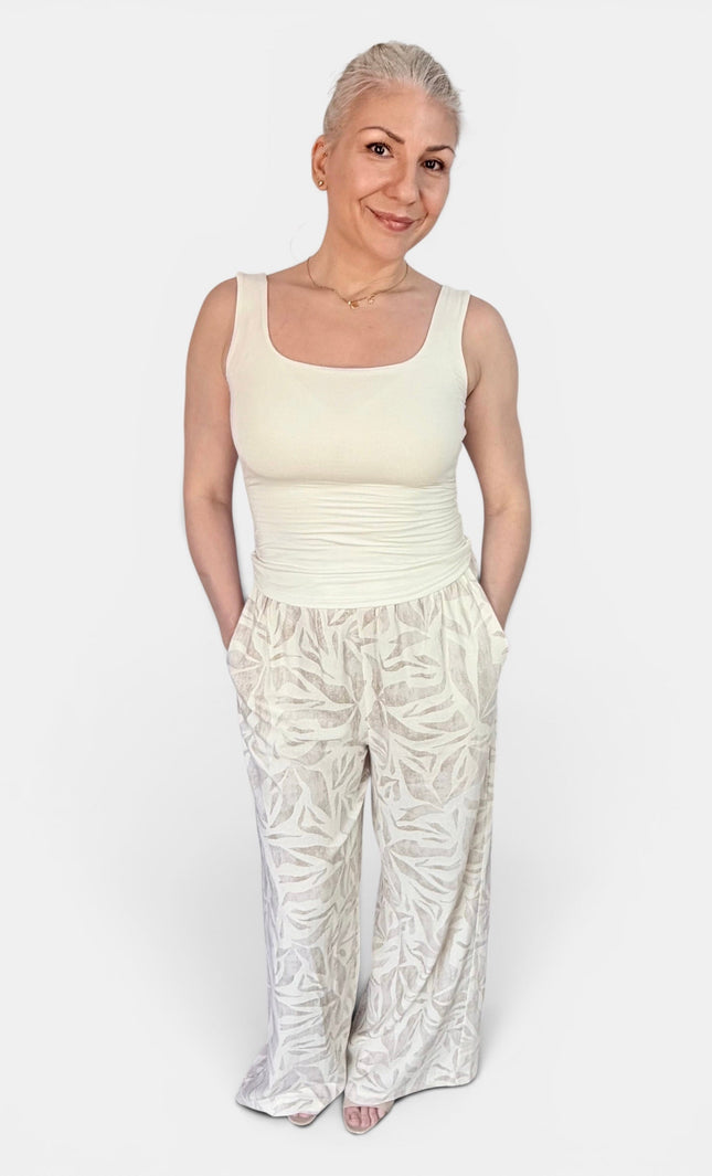 A woman modeling a cream-colored sleeveless top and matching cream patterned wide-leg pants against a plain light gray background.