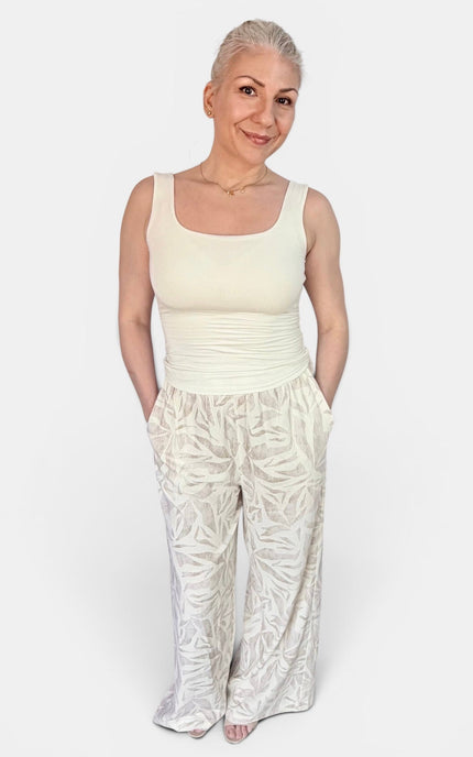 A woman modeling a cream-colored sleeveless top and matching cream patterned wide-leg pants against a plain light gray background.