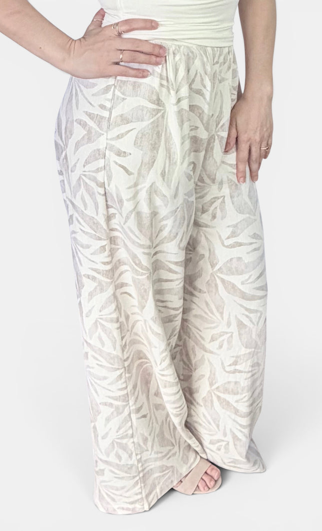 A person wearing loose, wide-leg pants with an allover tonal leaf pattern in off-white and beige, paired with a light top against a plain light background.