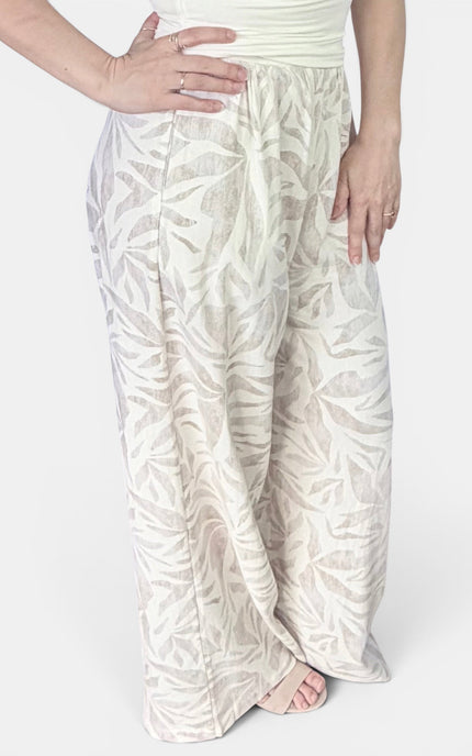 A person wearing loose, wide-leg pants with an allover tonal leaf pattern in off-white and beige, paired with a light top against a plain light background.