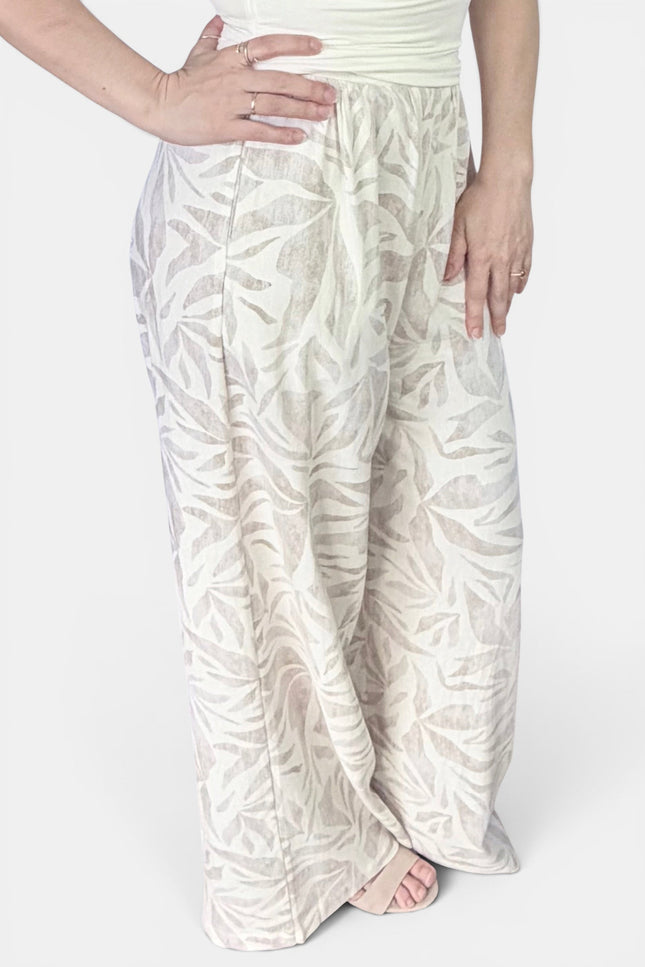 A person wearing loose, wide-leg pants with an allover tonal leaf pattern in off-white and beige, paired with a light top against a plain light background.