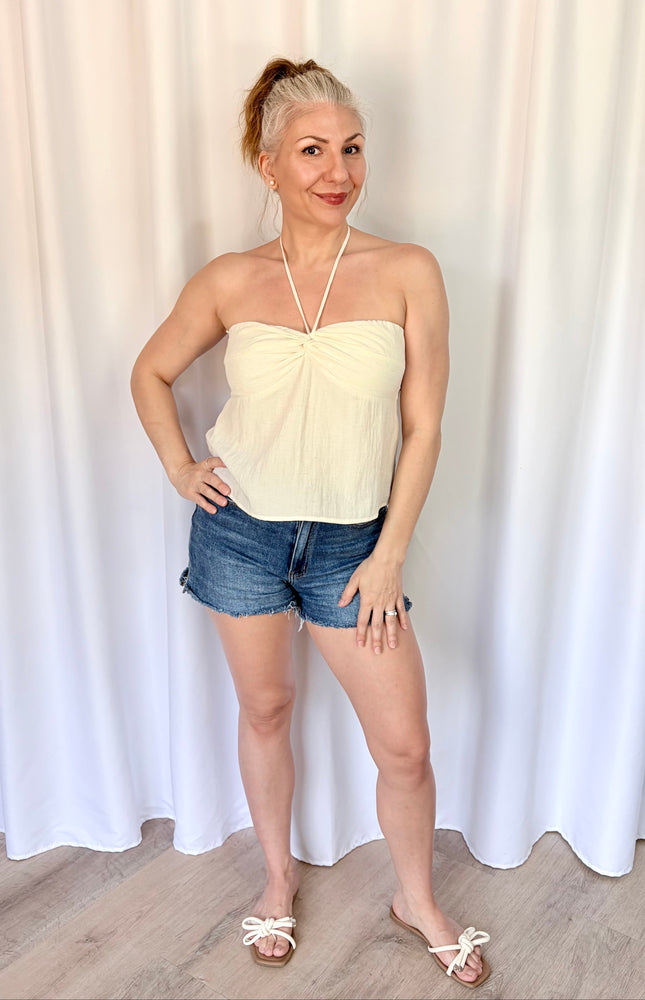 Woman wearing a strapless top and denim shorts against a white curtain background